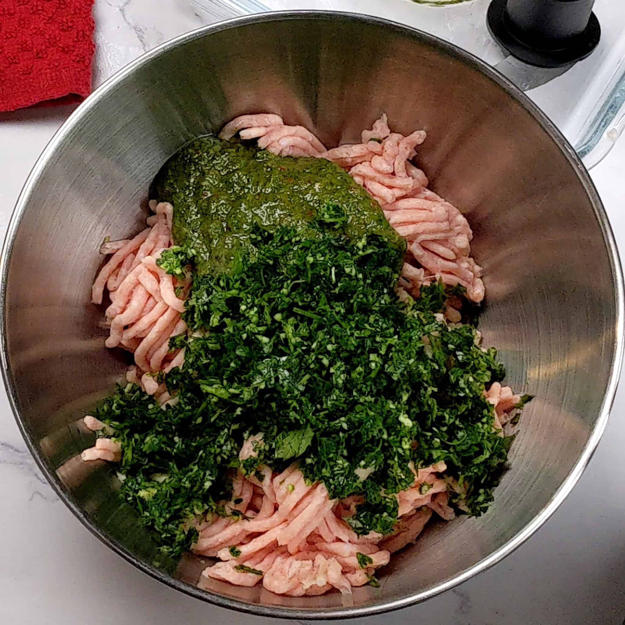 store bought ground chicken with zhug, and an aromatic paste of parsley, shallots and garlic in a stainless steel mixing bowl.