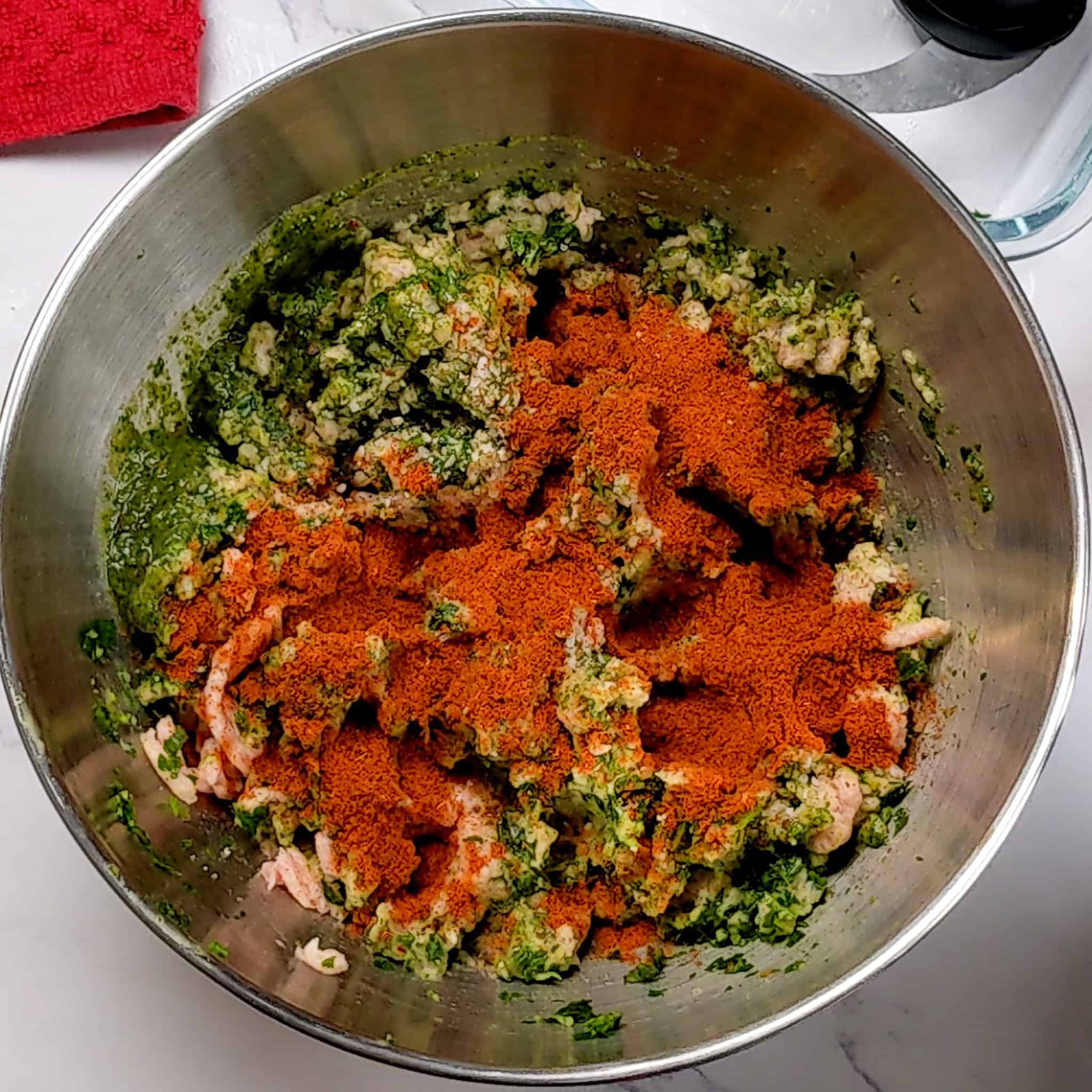 store bought ground chicken with zhug, and an aromatic paste of parsley, shallots and garlic in a stainless steel mixing bowl combined with baharat seasoning added.