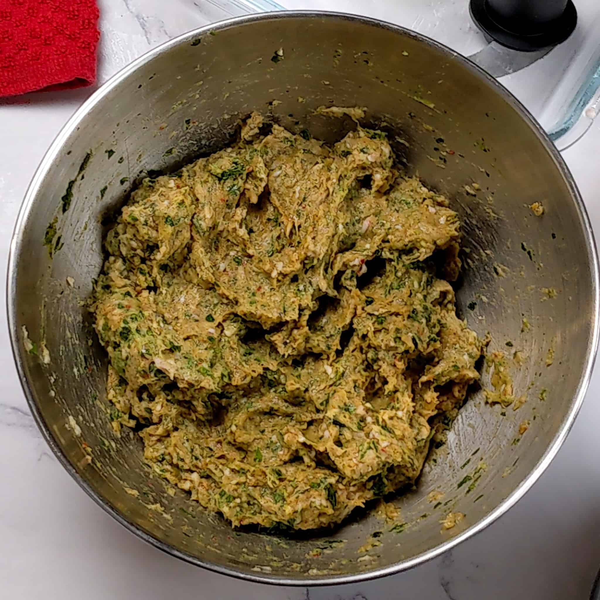 store bought ground chicken with zhug, and an aromatic paste of parsley, shallots and garlic in a stainless steel mixing bowl with baharat seasoning added combined.