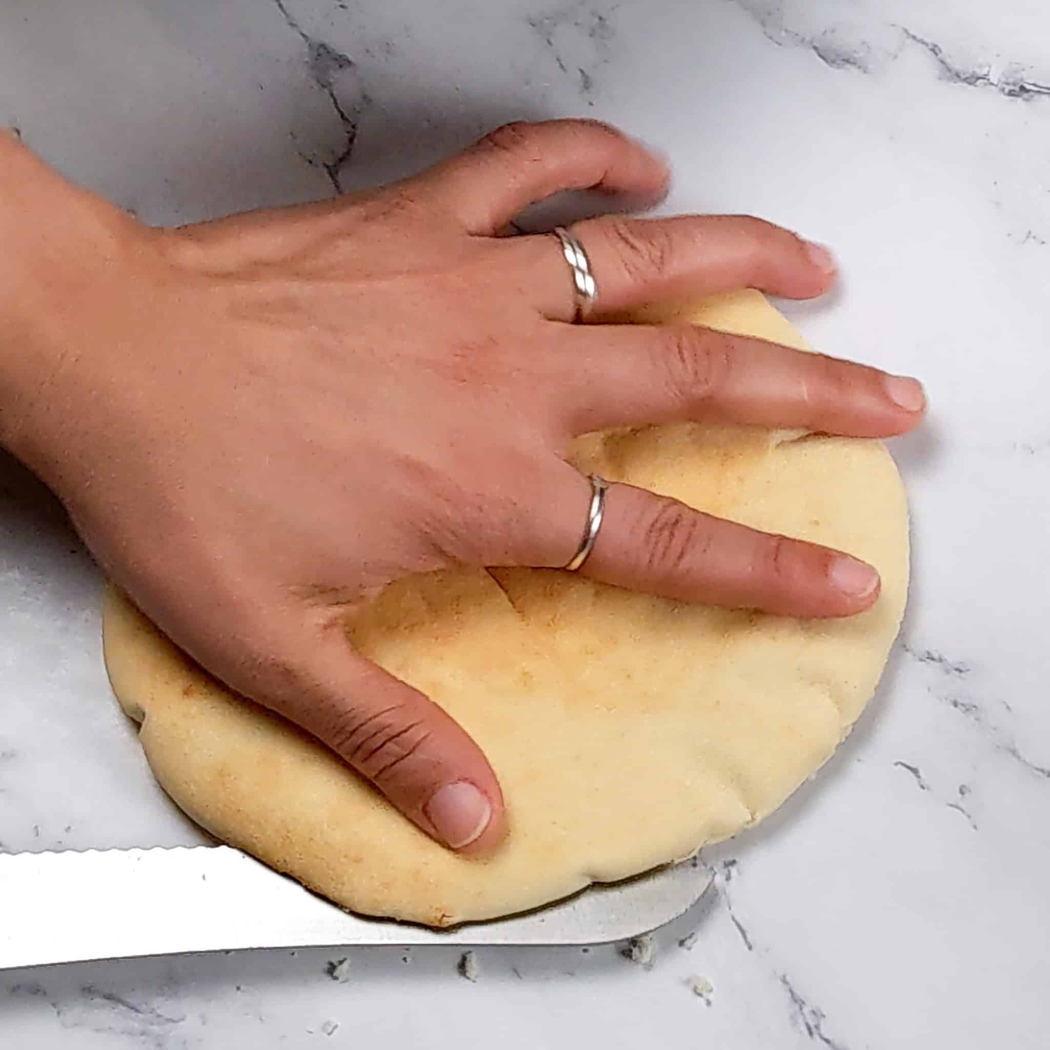 one pita bread being spit into halves with a bread knife.