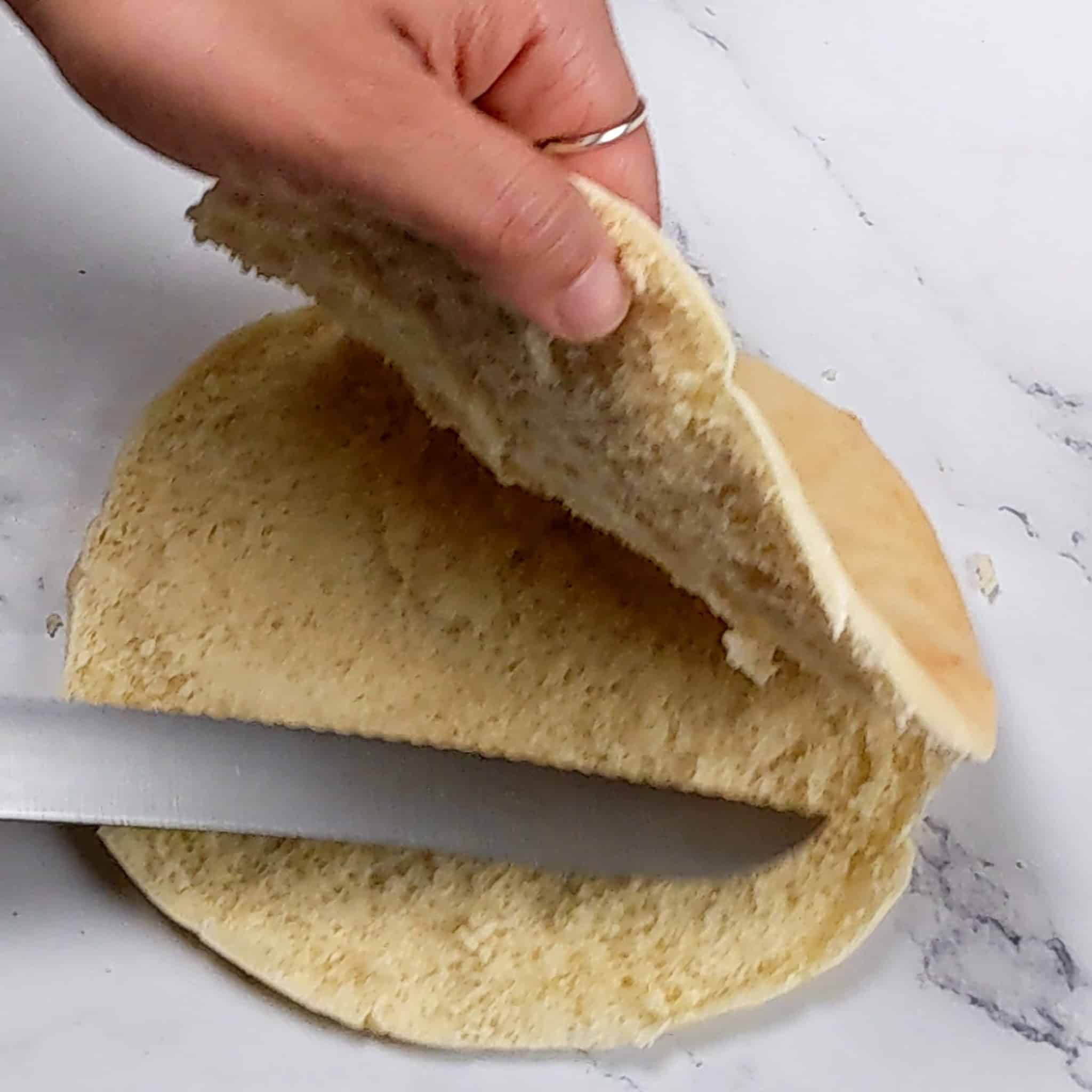 the top layer of the pita bread being pulled back while the knife finishes cutting the pita in half.