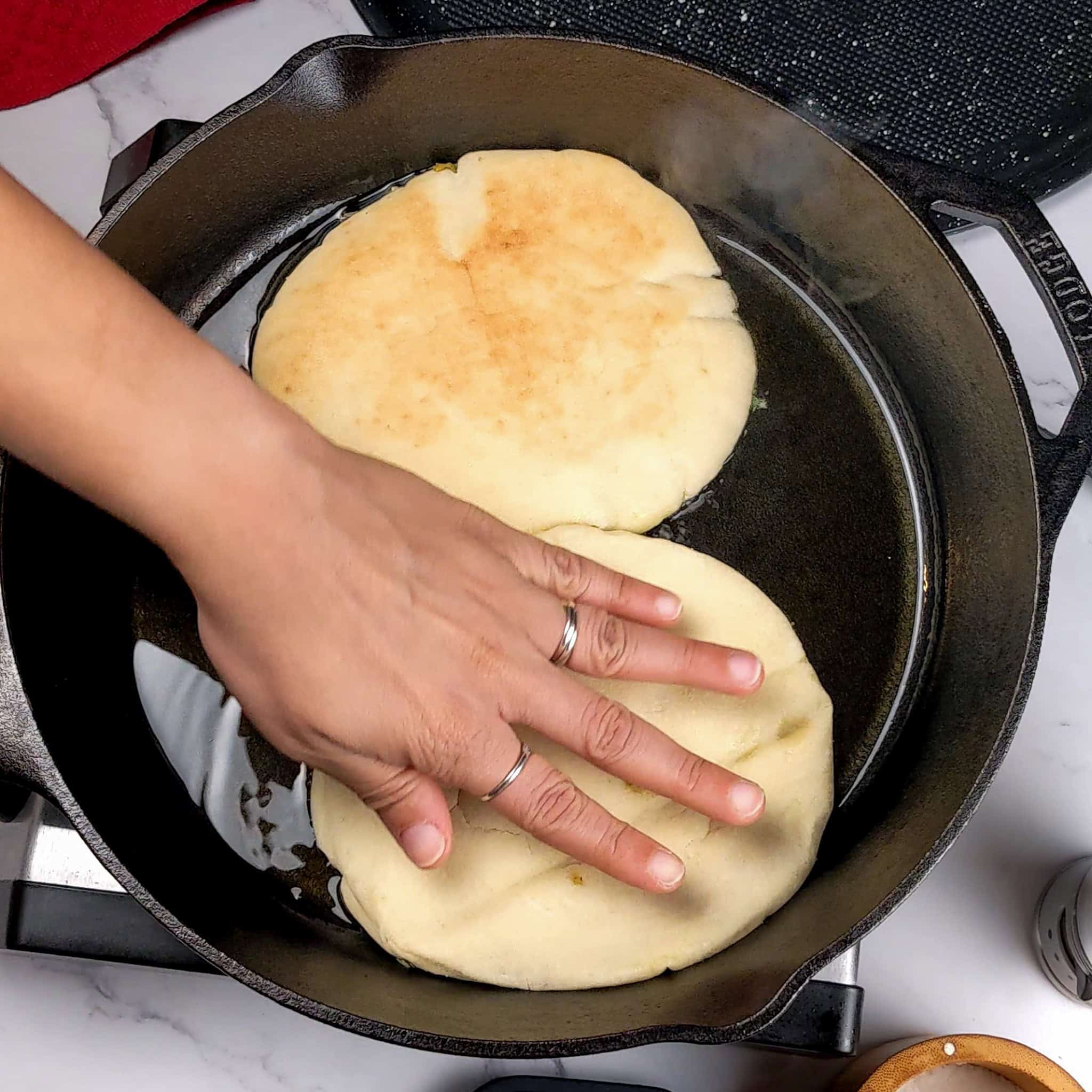 pita smeared with the chicken mixture being pressed by hand face down in a lodge cast iron skillet.