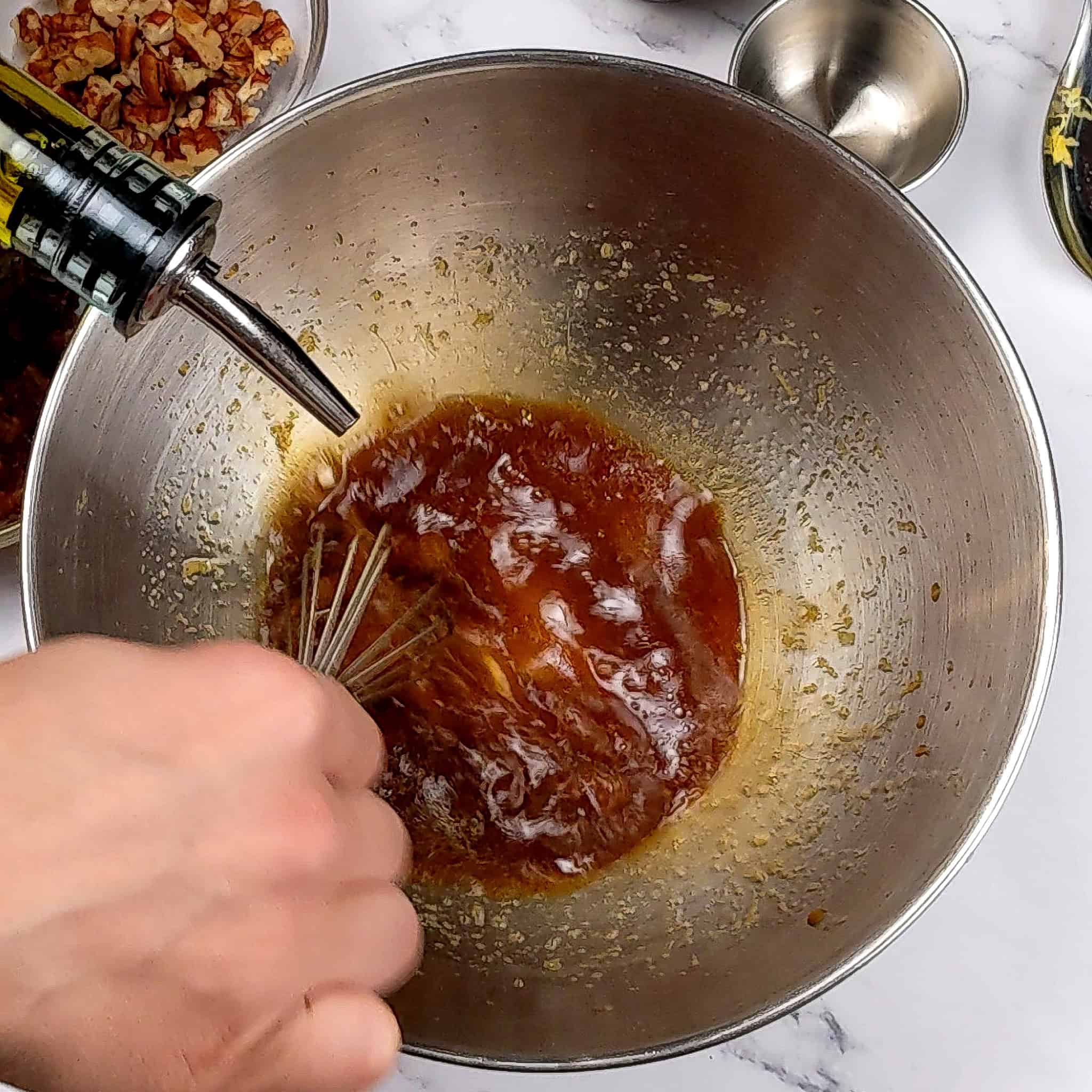 vinaigrette being made while oil is being poured in while the other hand is whisking in a stainless steel mixing bowl.