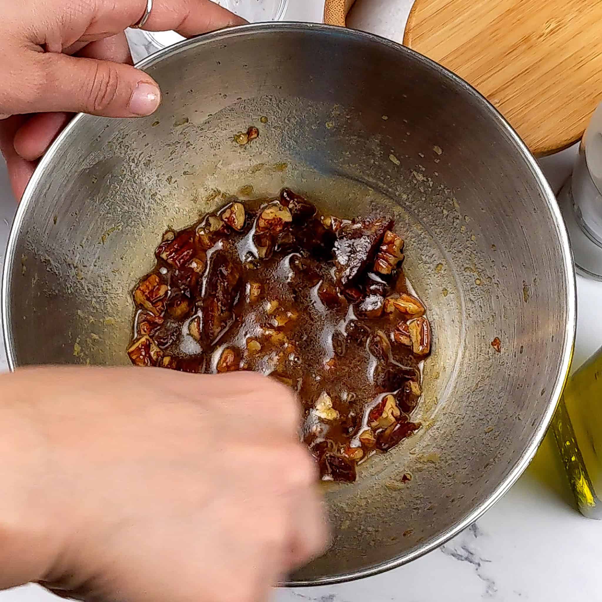 the pomegranate vinaigrette combined with pecans and dates in a stainless steel bowl.