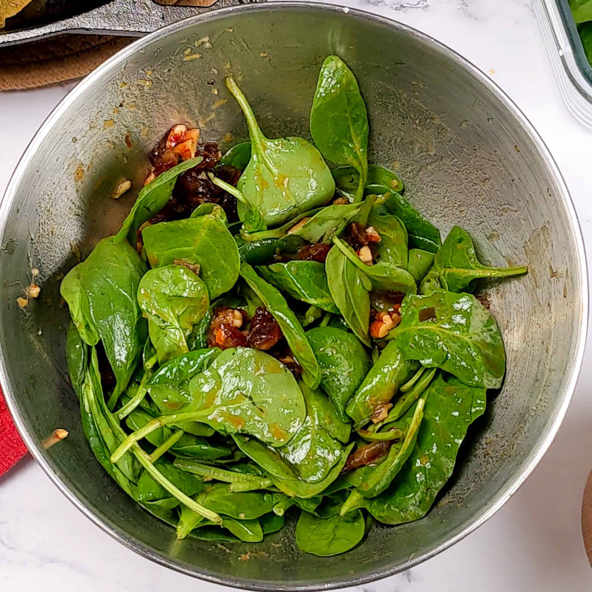 spinach added to the pomegranate date and pecans dressing in a mixing bowl.