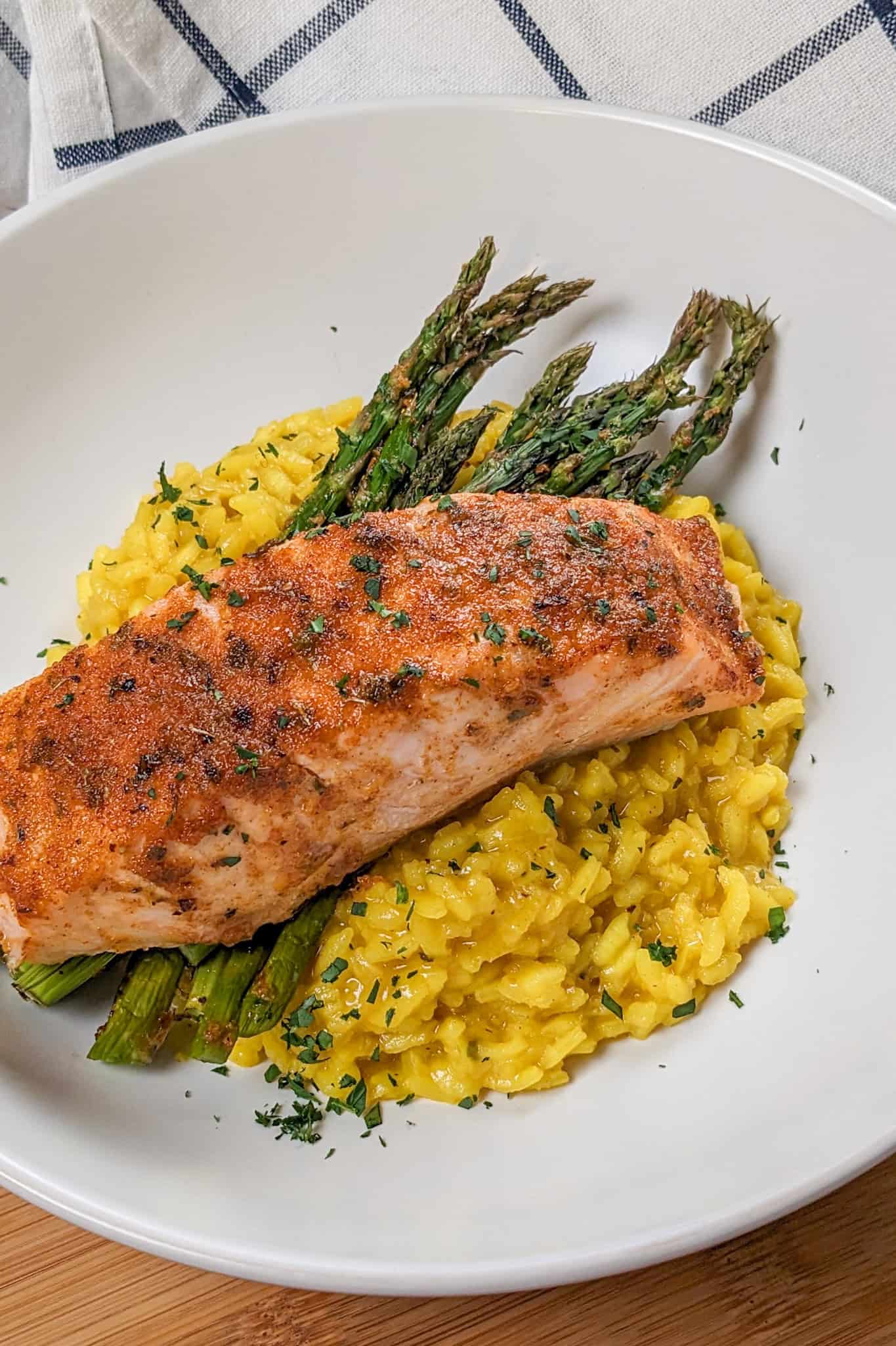 top view of the Best Air Fryer Habanero Adobo Salmon and Yellow Risotto with asparagus on a round wide rim bowl next to a kitchen towel