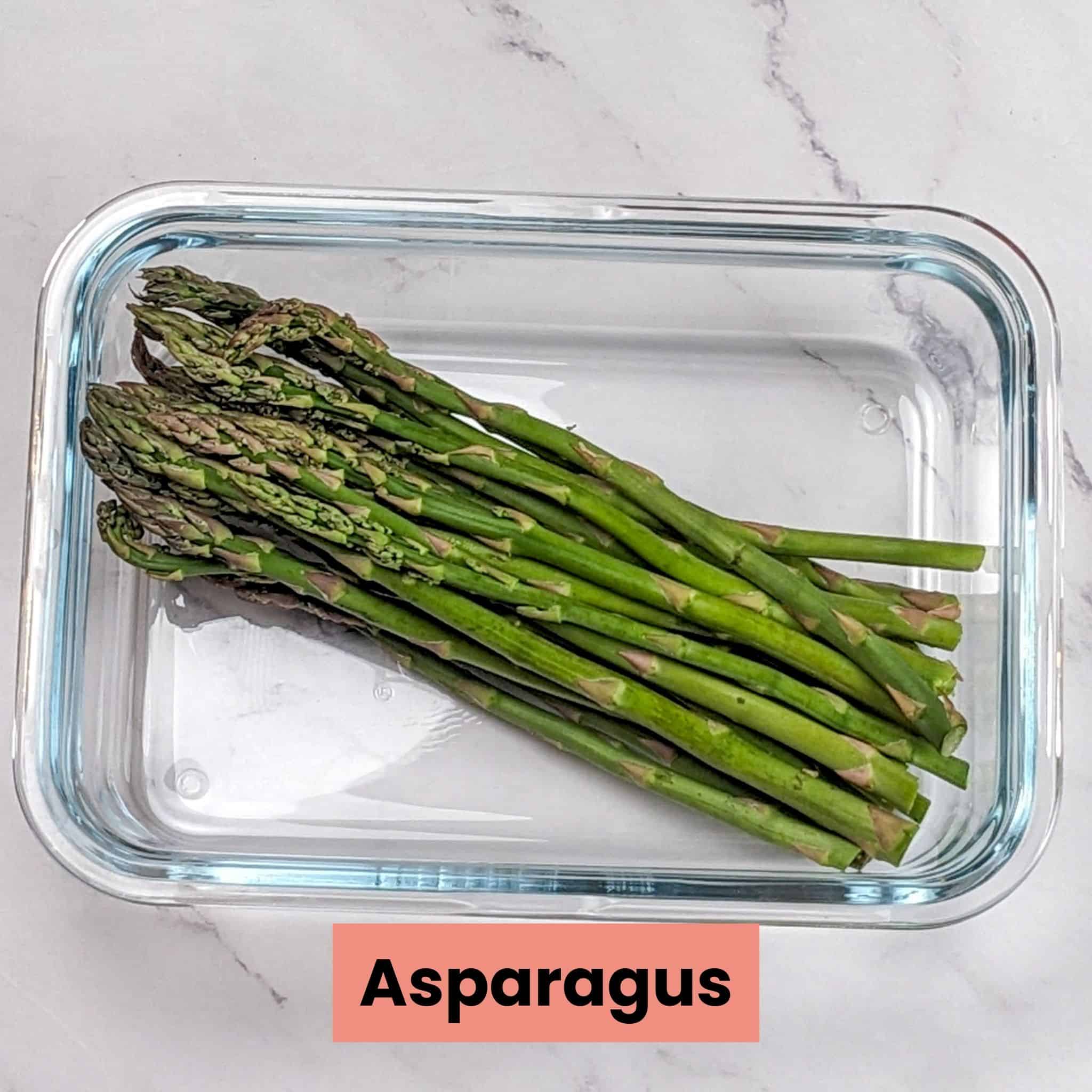 raw asparagus with the bottoms removed in a glass rectangle container.