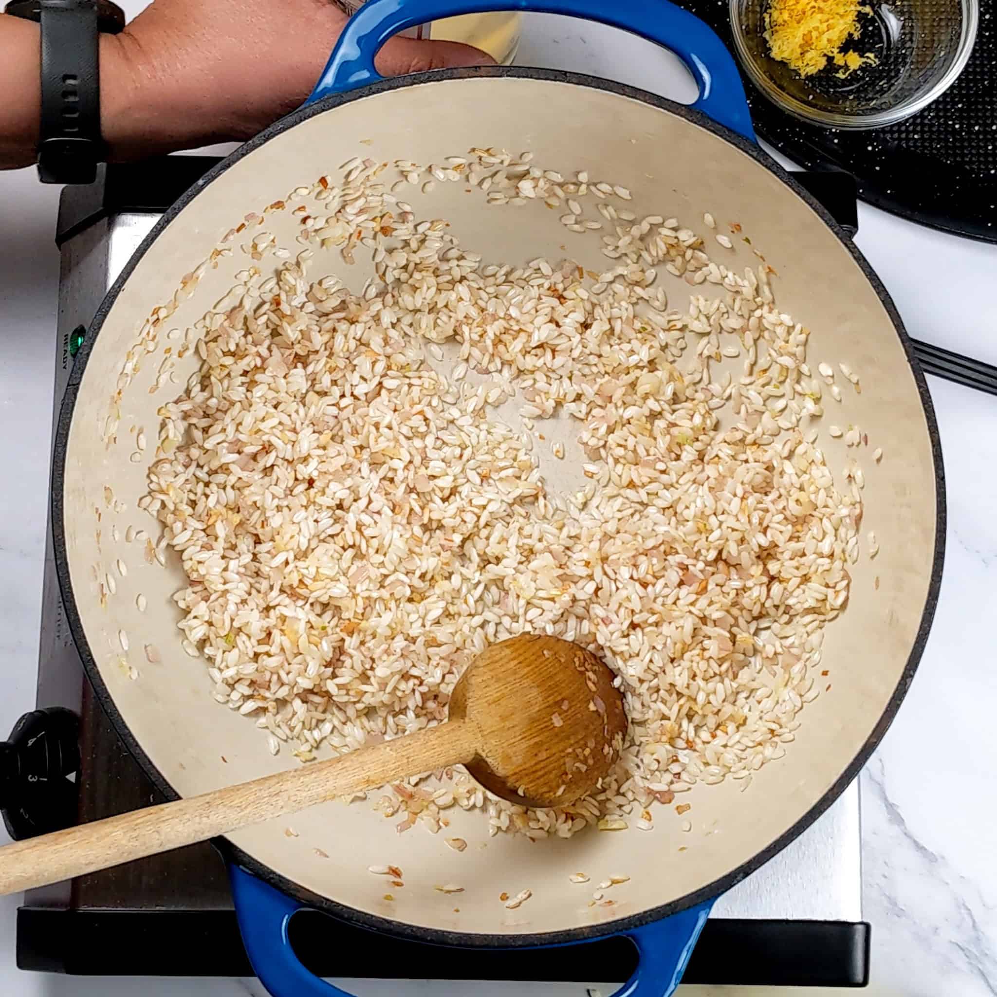 arborio rice with shallots and garlic cooking in a dutch oven.