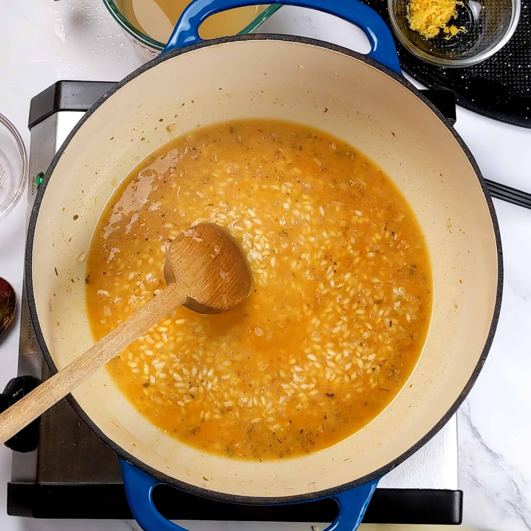 chicken broth with arborio rice in a dutch oven with a wooden spoon laying in it.