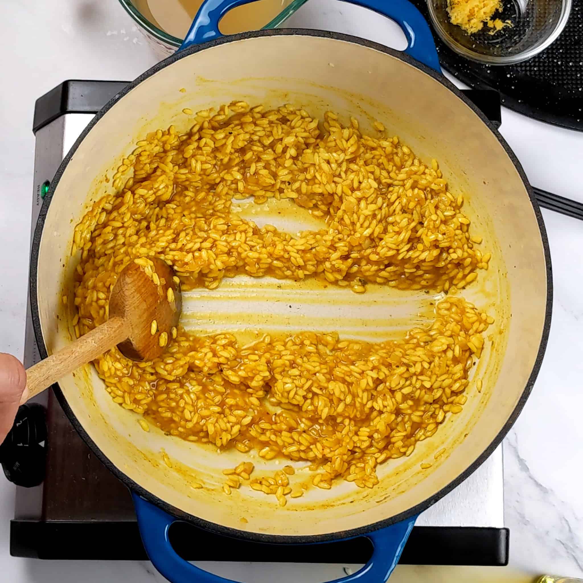 the chicken broth absorbed puffed up yellow arborio rice split into two with a wooden spoon in lodge dutch oven.