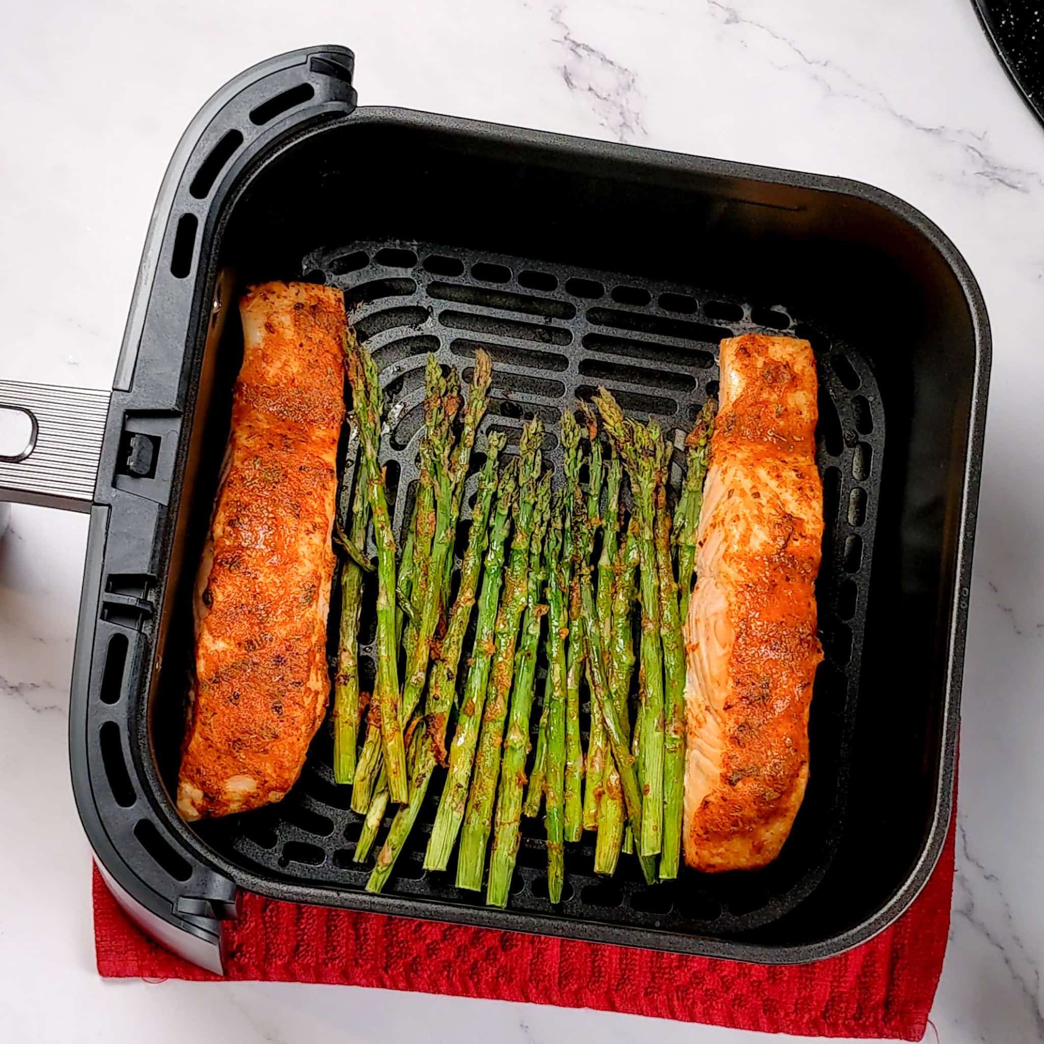 The cooked asparagus and salmon in a the air fryer basket, resting on a square kitchen towel.