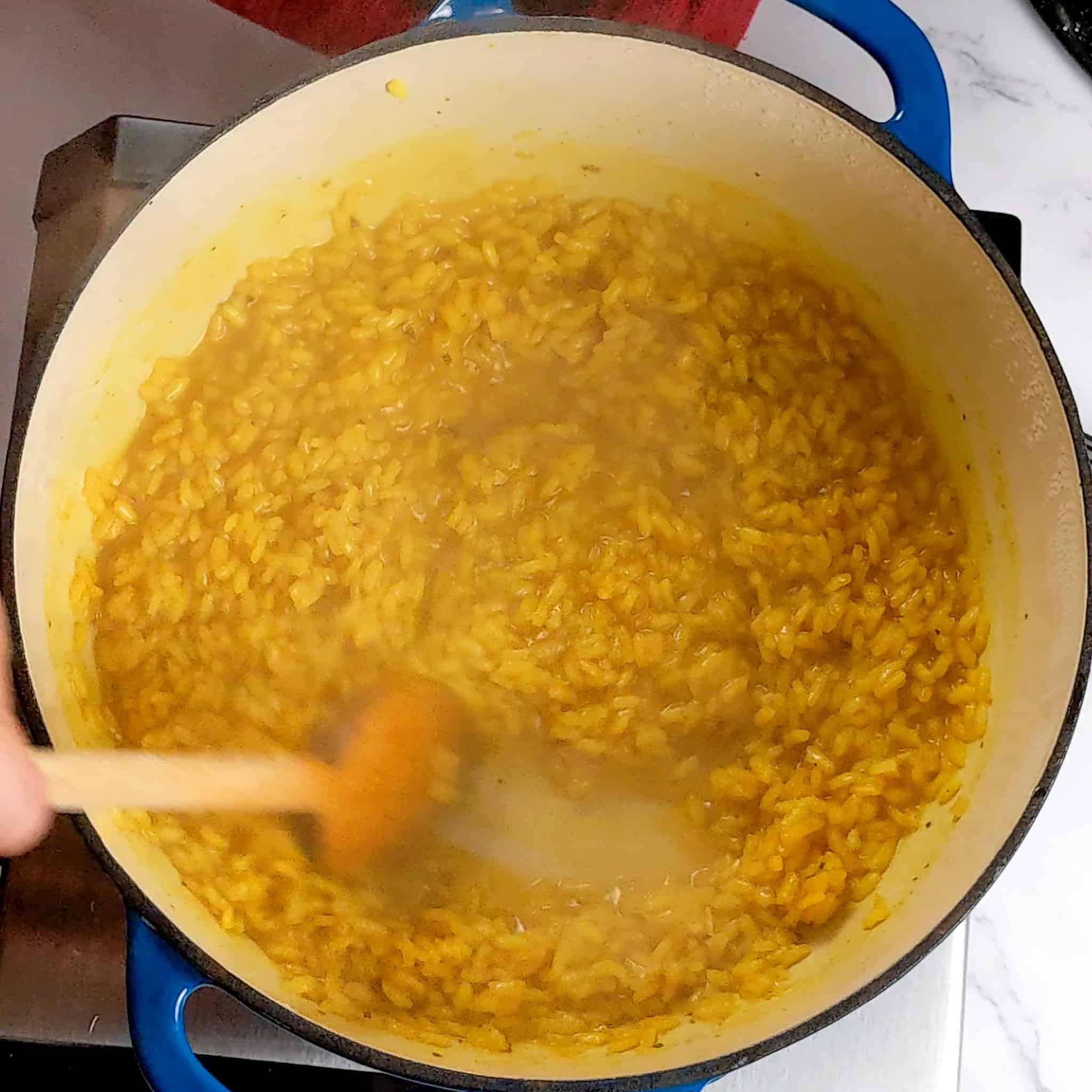 a wooden spoon scrapping the bottom of the pan in one streak to show that the liquid in the risotto is absorbed.