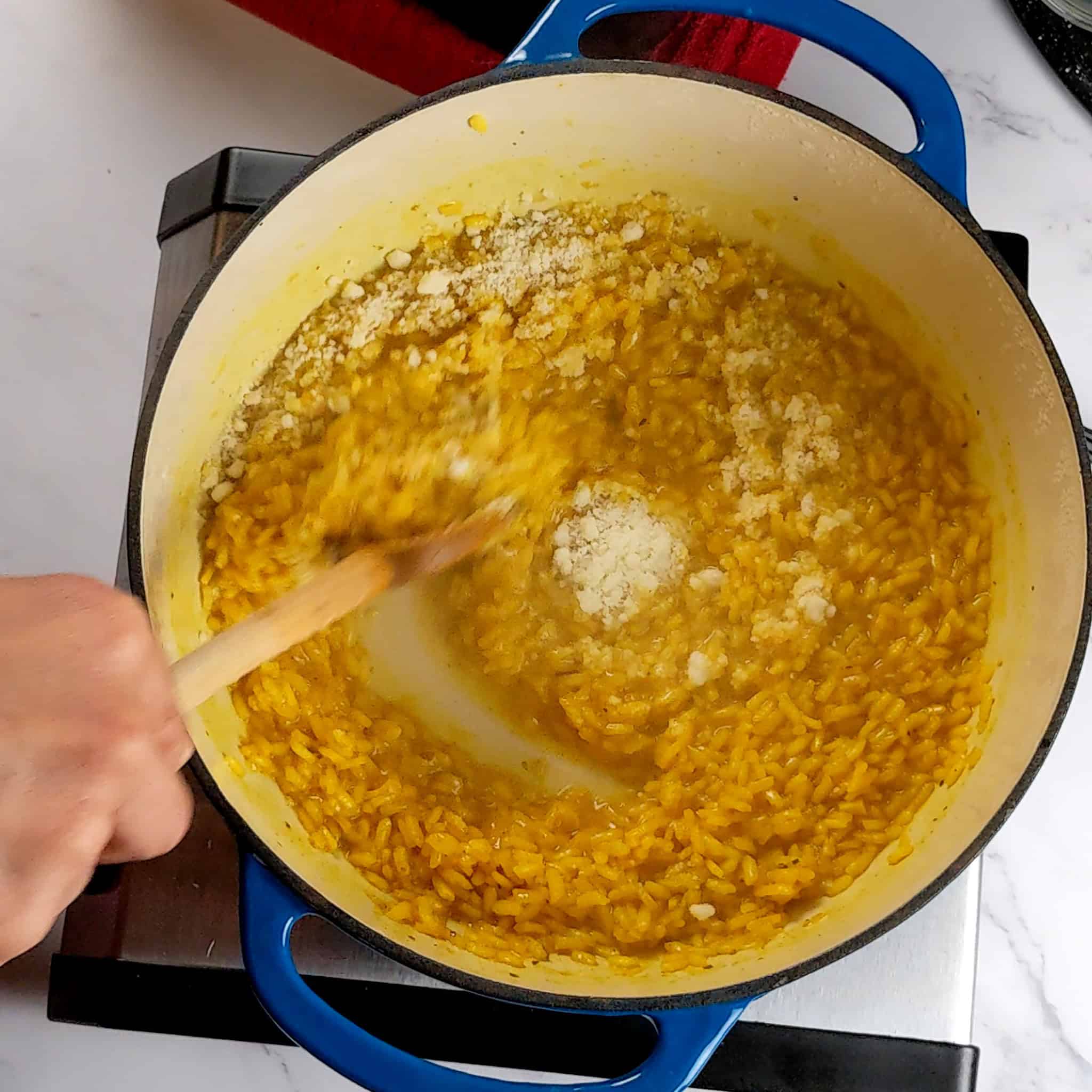 grated pecorino cheese being mixed into the yellow risotto with a wooden spoon.