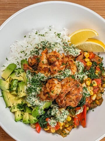 Top view of the Spicy Cajun Shrimp Rice Bowl with Lemon Remoulade in a wide rim bowl with diced avocado and lemon wedges.
