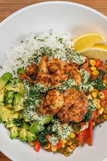 Top view of the Spicy Cajun Shrimp Rice Bowl with Lemon Remoulade in a wide rim bowl with diced avocado and lemon wedges.