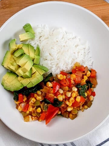 diced avocado added to the wide rim bowl of jasmine rice and vegetable medley.