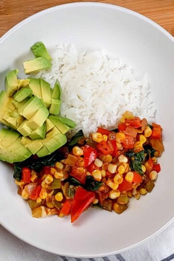 diced avocado added to the wide rim bowl of jasmine rice and vegetable medley.