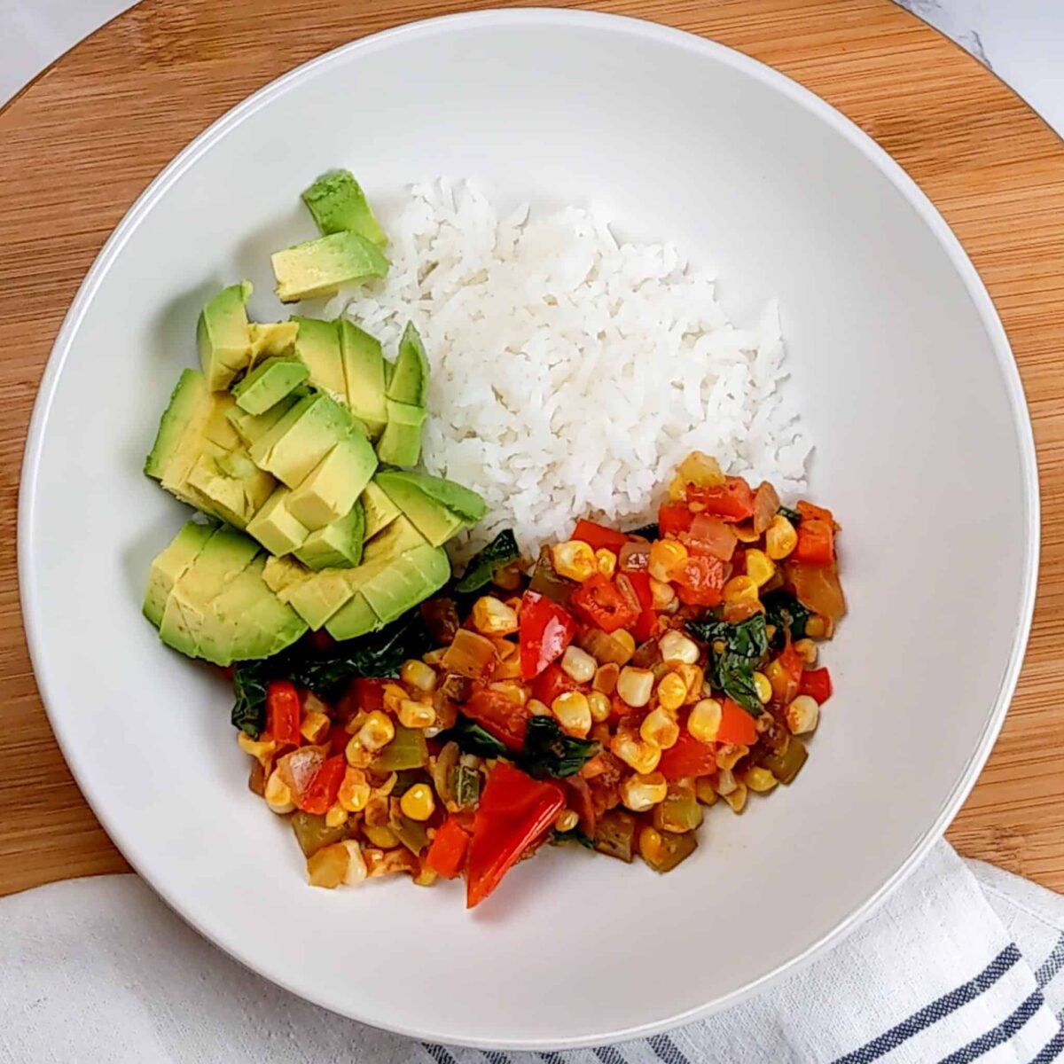 diced avocado added to the wide rim bowl of jasmine rice and vegetable medley.