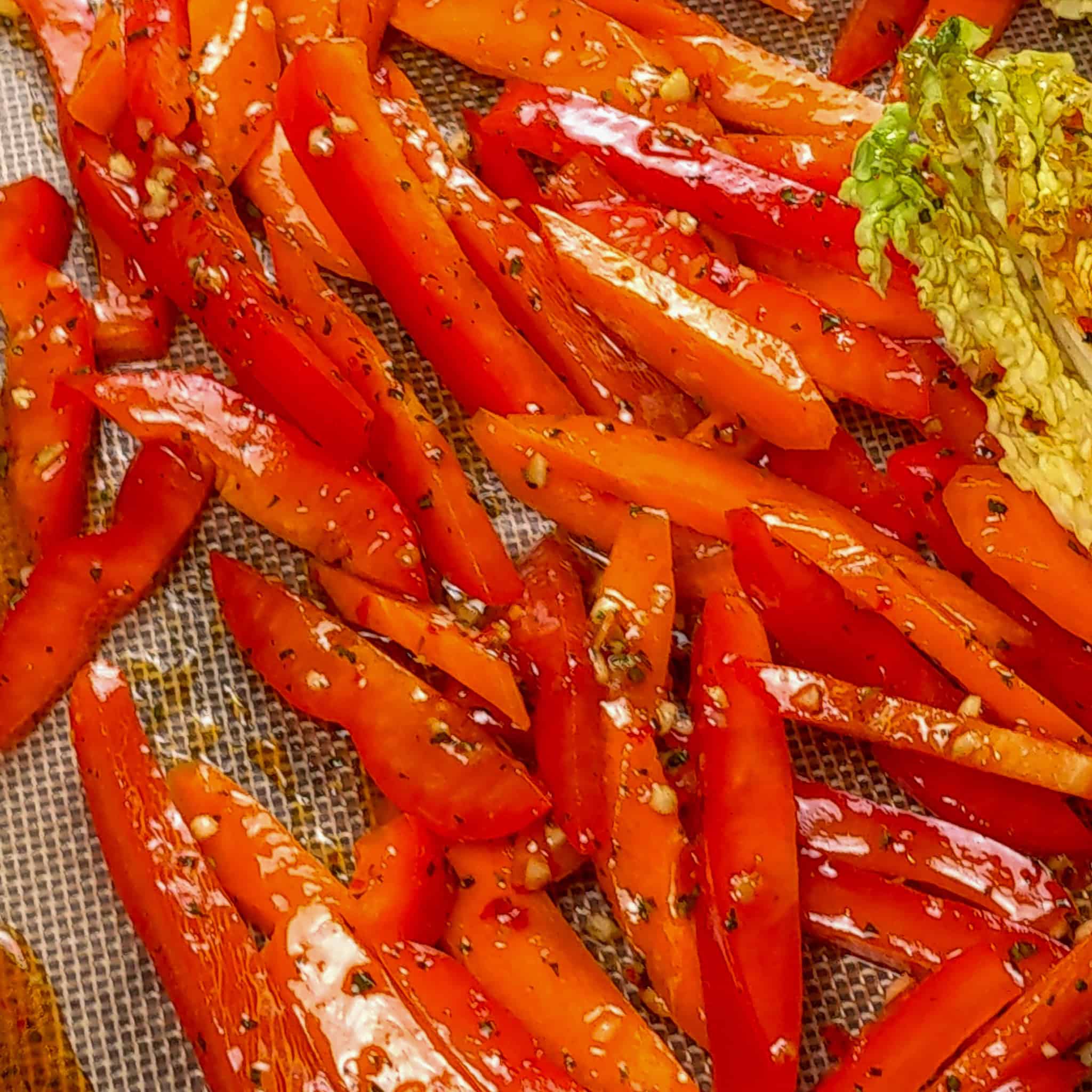 close up of the mixed red bell pepper and carrot strips on the sheet pan tossed in the wet seasoning.