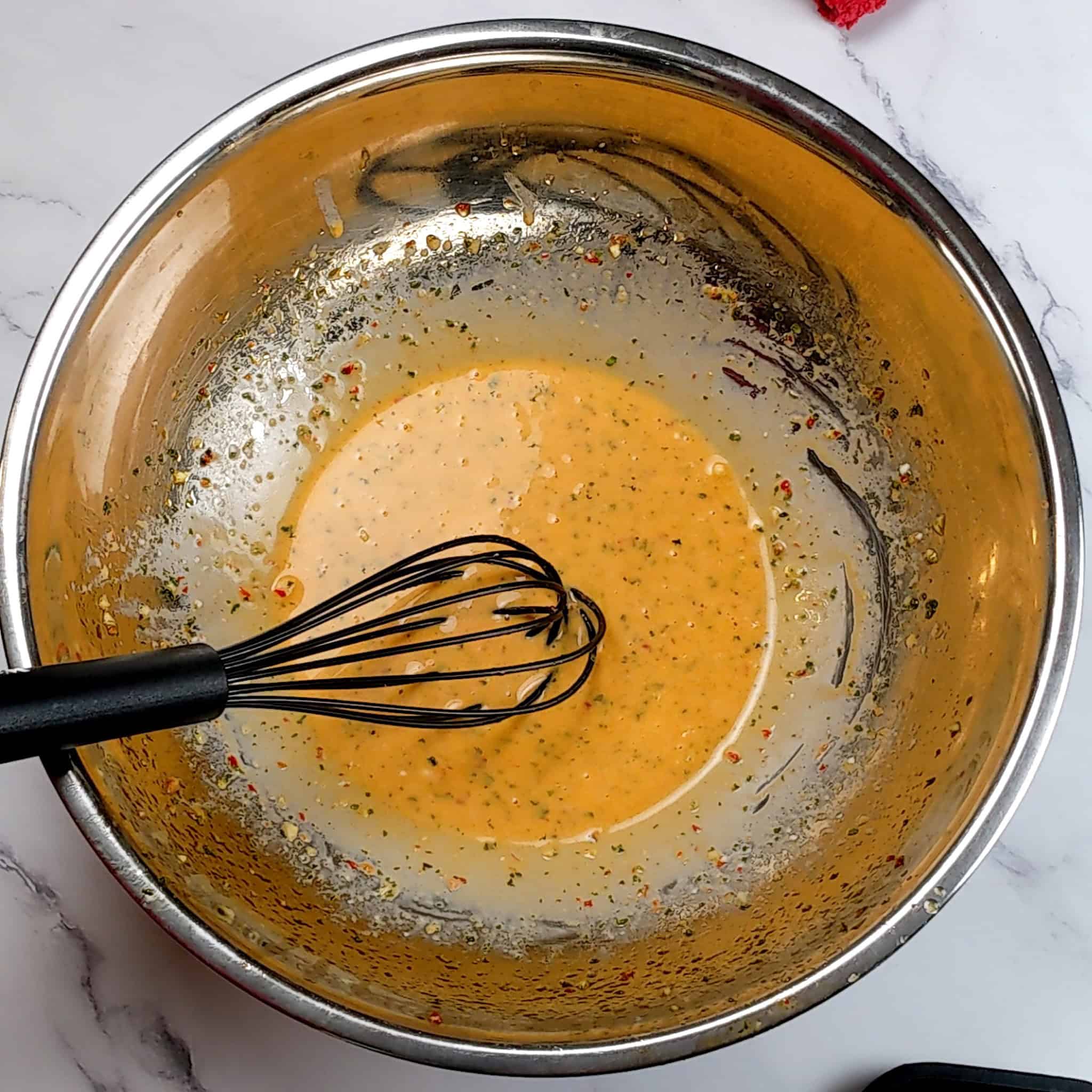 a bowl with the reserved wet seasoning that was whisked with mayonnaise with the silicone whisk resting in the bowl.