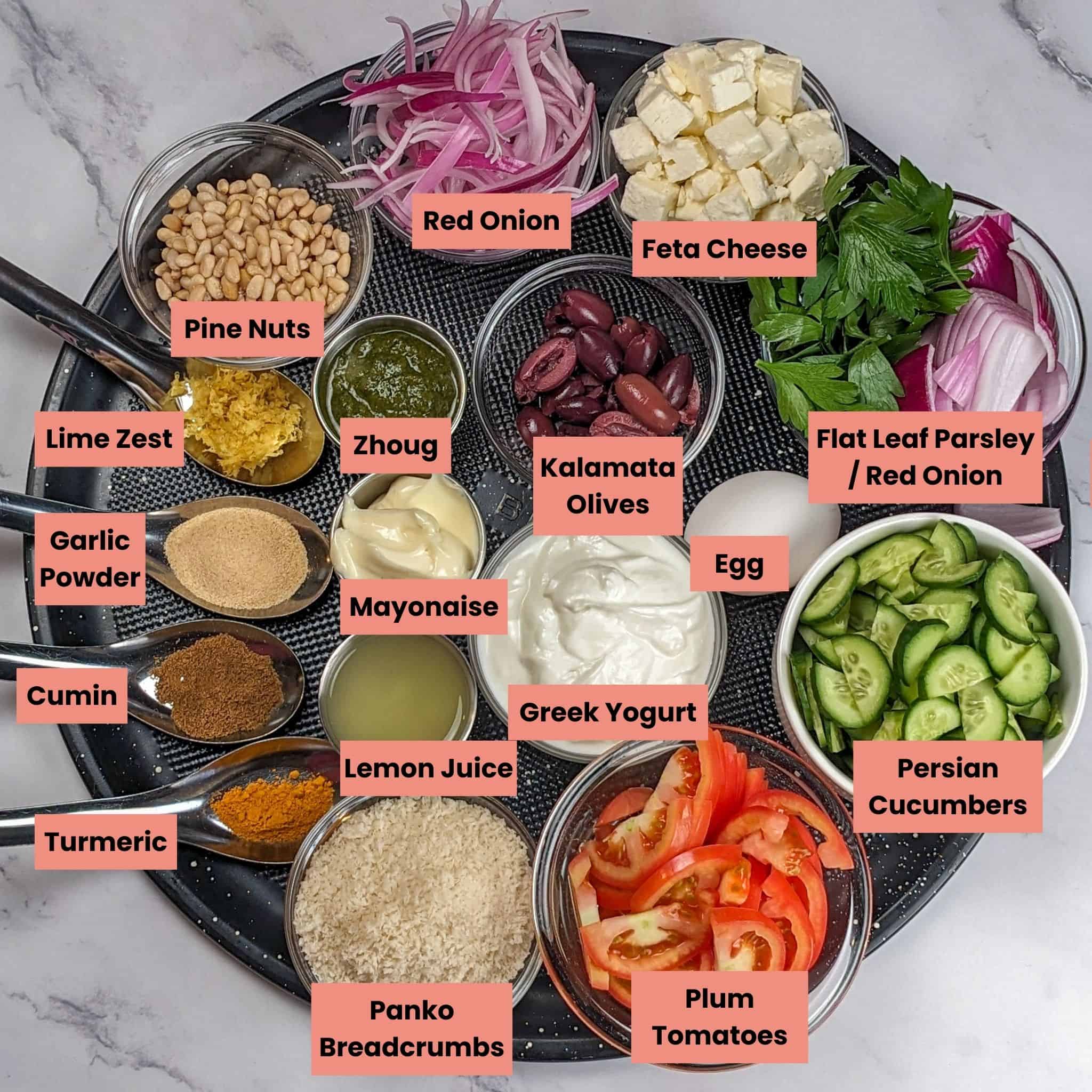 Labeled ingredients for the Spicy Greek Chicken Meatball Rice Bowl in glass and stainless steel containers and spoons on a large round pizza pan.