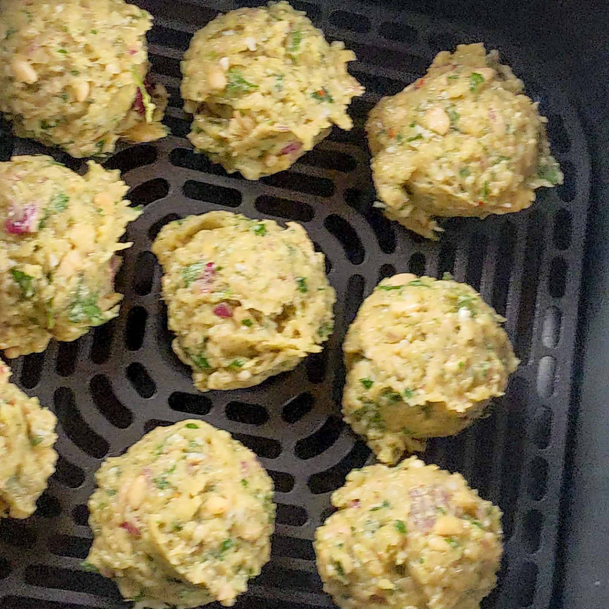 evenly spaced out raw chicken meatballs in an air fryer basket.