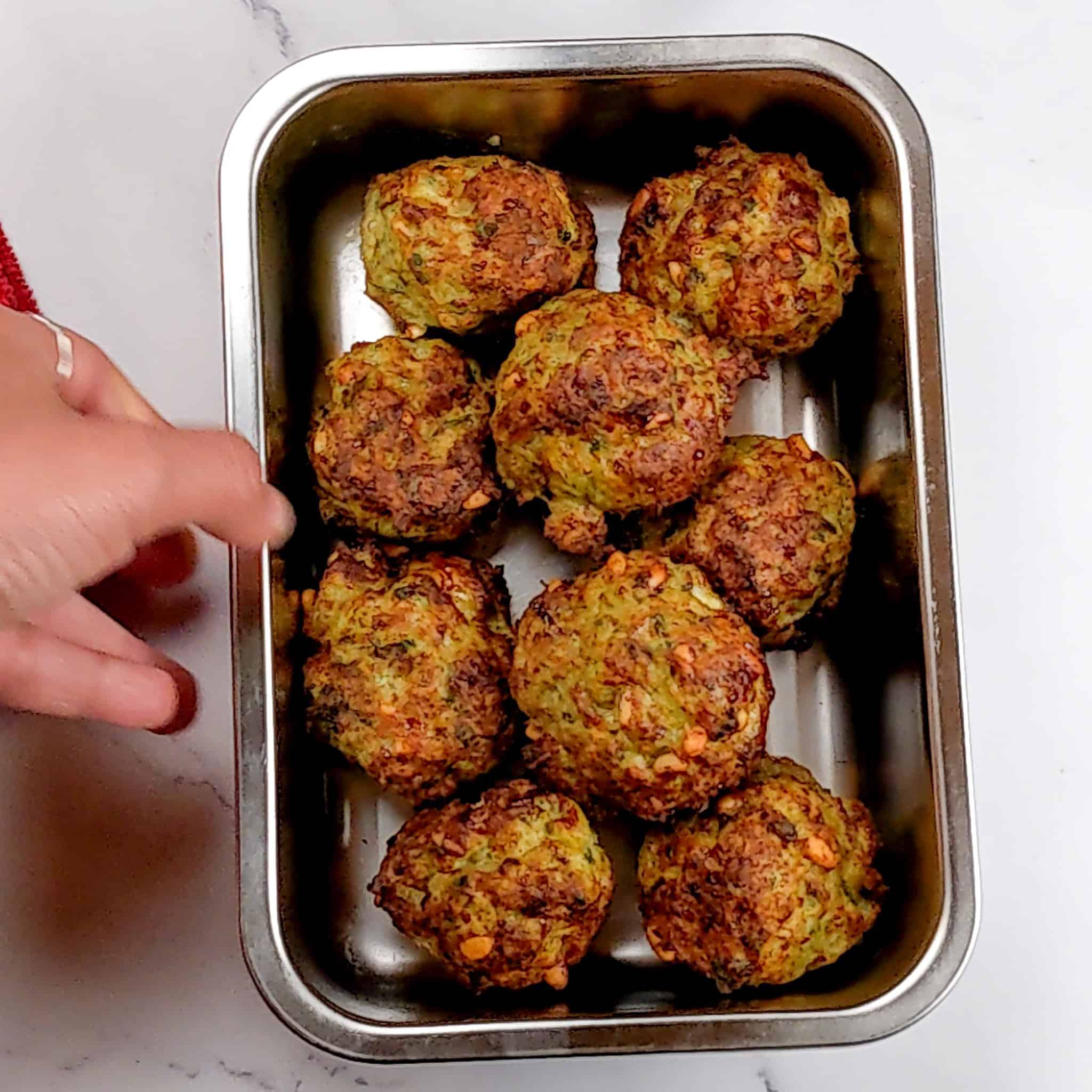 cooked golden brown meatballs piled in a rectangle metal container.