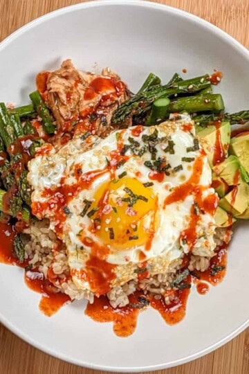 the Easy Sheet Pan Spicy Miso Salmon Rice Bowl in a wide rim bowl drizzled with siracha, sesame oil and salmon furikake seasoning.