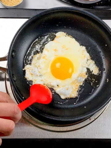 sesame seeds and oil being spooned over the fried sunny side egg with a silicone spoon made by GIR.