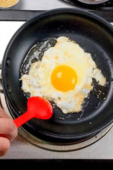 sesame seeds and oil being spooned over the fried sunny side egg with a silicone spoon made by GIR.