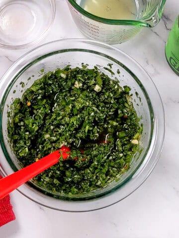 jalapeno chimichurri sauce in a glass mixing bowl with a silicone spoon.