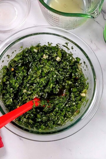 jalapeno chimichurri sauce in a glass mixing bowl with a silicone spoon.