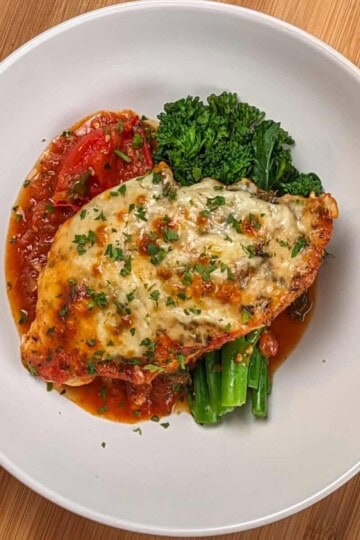 Baked Cheesy Spicy Tomato Basil Chicken and Broccolini on a wide rim bowl.