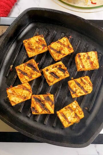 marinated tofu grilling in a grill pan, flipped and showing grill marks.