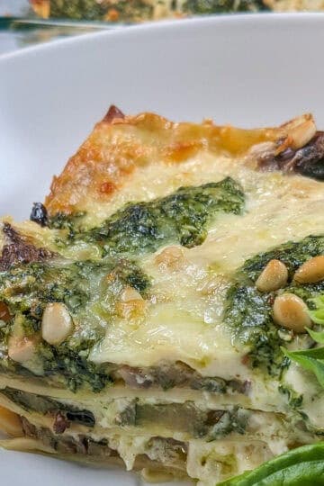 side view of the baked lasagna garnished with more pine nuts and basil.