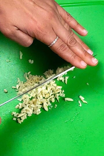 Close-up of garlic chopping on a vibrant green cutting board with a sharp knife.