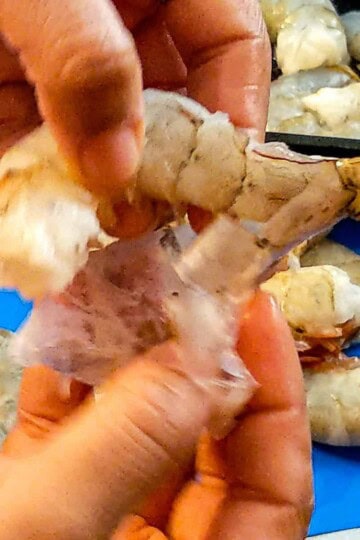 the shell of the shrimp being peel with two hands.
