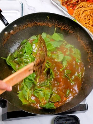 Sautéed spinach in wok complements Caribbean beef noodle soup preparation for a flavorful meal.
