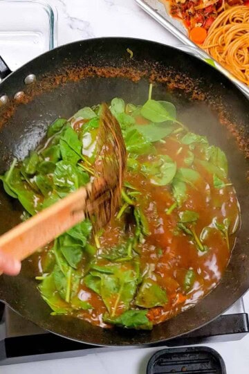 Sautéed spinach in wok complements Caribbean beef noodle soup preparation for a flavorful meal.