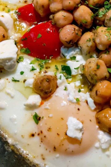 Vibrant eggs and chickpeas skillet topped with feta, red peppers, and fresh herbs.