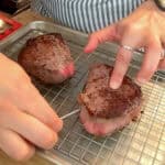 Meat thermometer checks medium-rare steak on a cooling rack in a cozy kitchen.