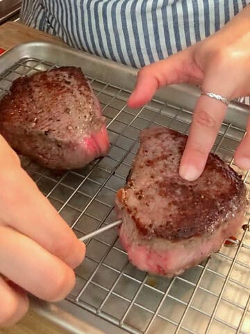 Meat thermometer checks medium-rare steak on a cooling rack in a cozy kitchen.
