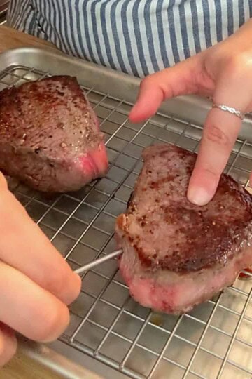 Meat thermometer checks medium-rare steak on a cooling rack in a cozy kitchen.