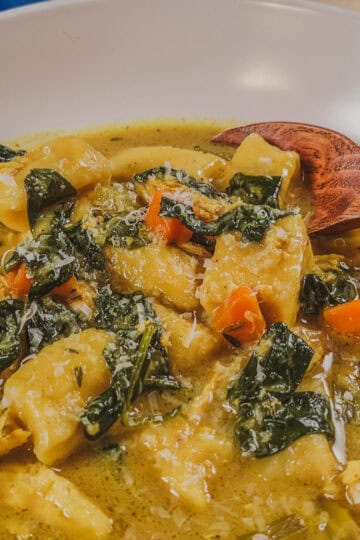 Homemade curry coconut chicken gnocchi soup with colorful vegetables and herbs.