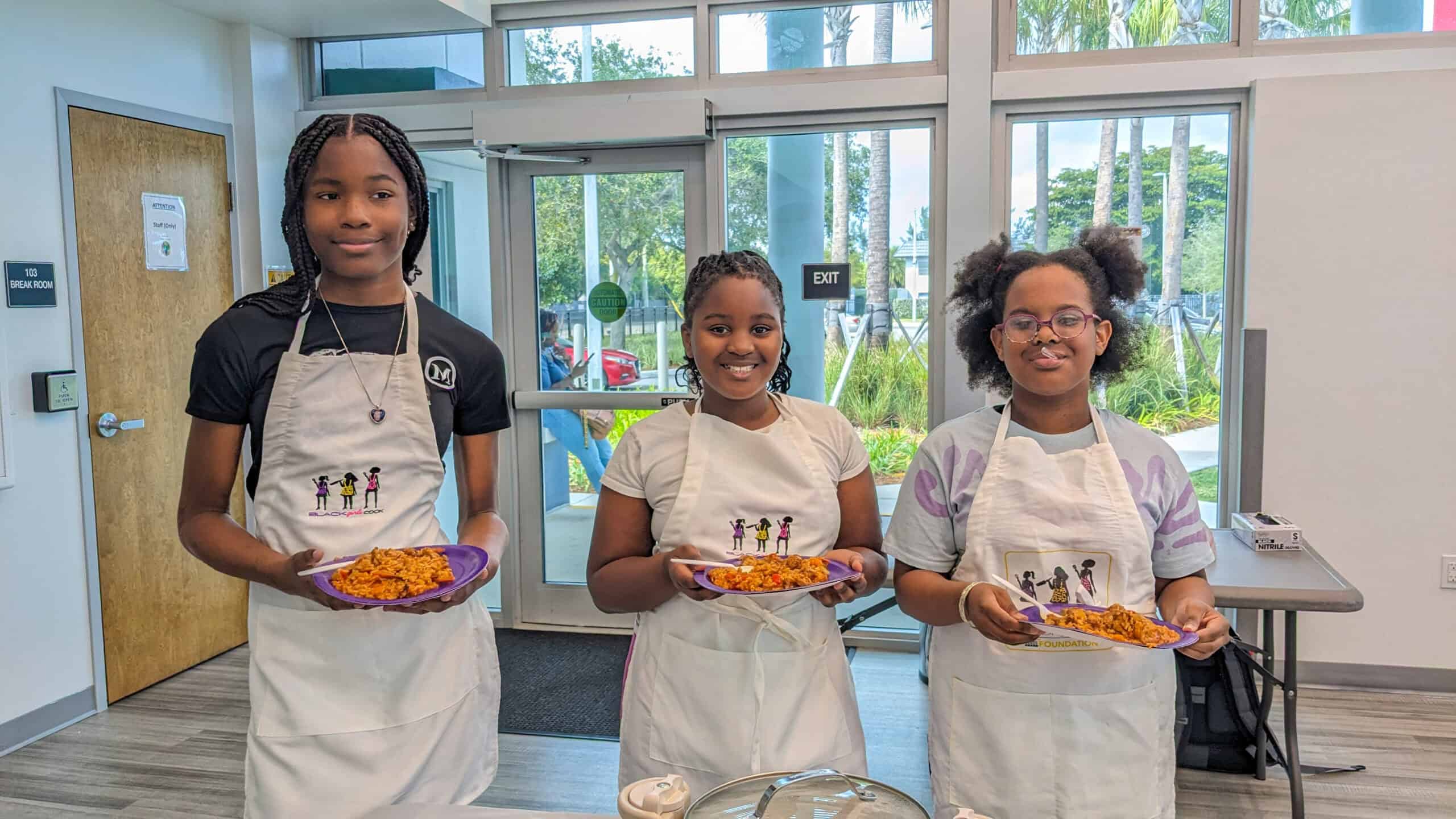 three young smiling girls holding plates of chicken shrimp jambalaya that they made in the class.