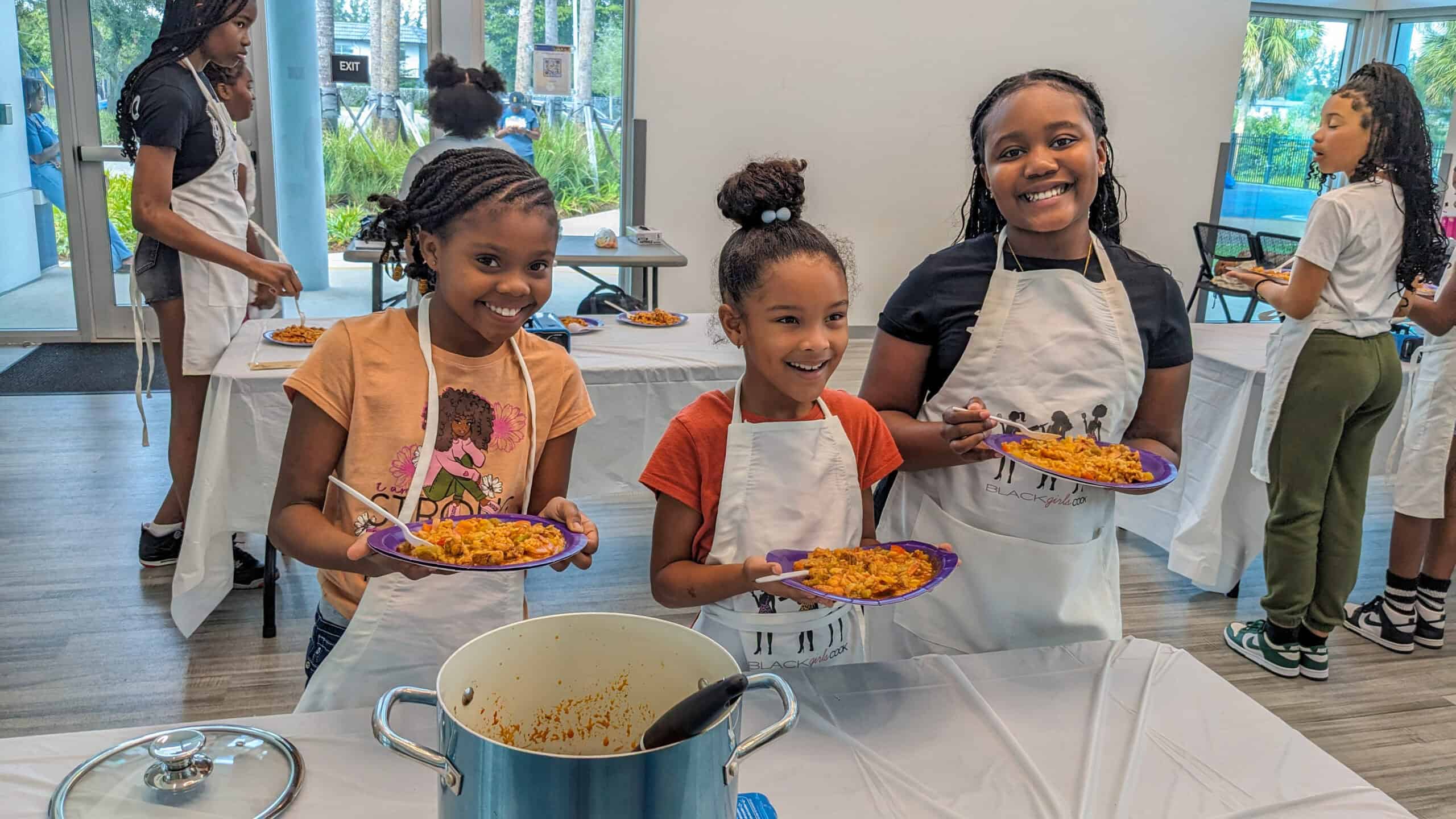 three young smiling girls holding plates of chicken shrimp jambalaya that they made in the class.