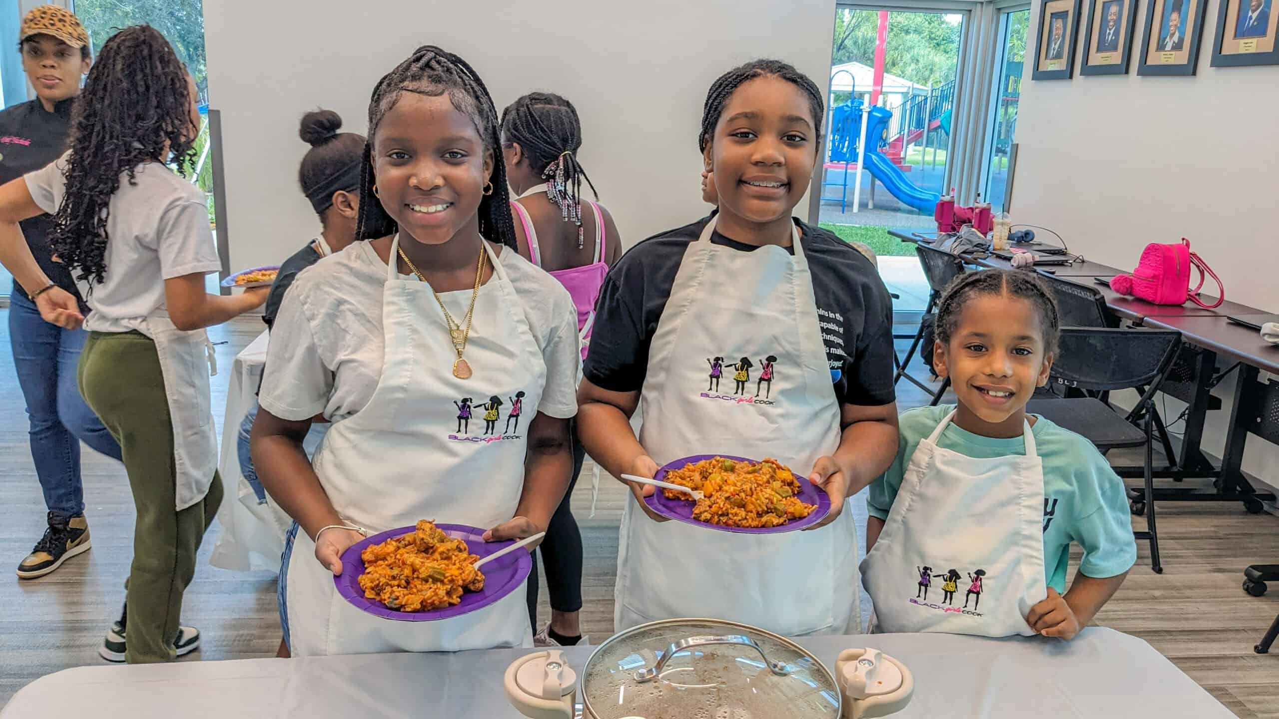 three young smiling girls holding plates of chicken shrimp jambalaya that they made in the class.