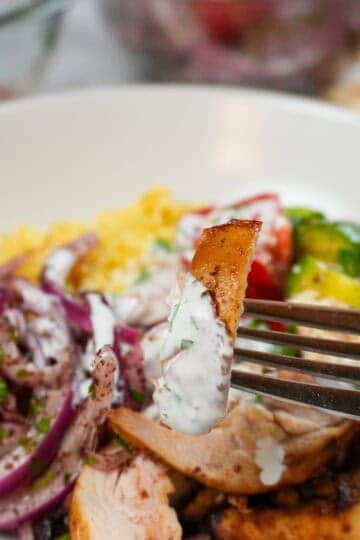 Air Fryer Shawarma Chicken Rice Bowl Beituti in a wide rim bowl with a fork and knife. with close up of the shawarma chicken drizzled with lemon greek yogurt dressing.