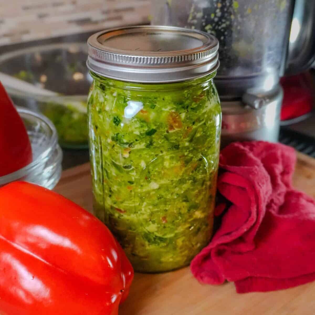 epis in a glass mason jar with kitchen equipment in the background and with whole red bell pepper laid next to it.