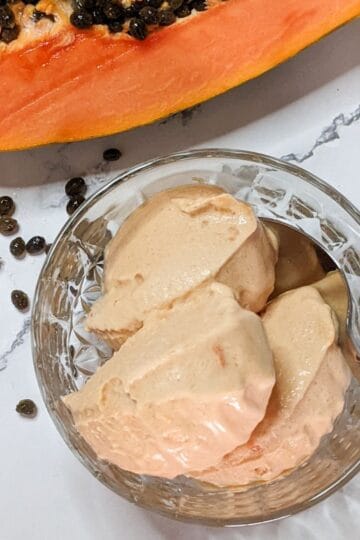 Delicious papaya ice cream served in a bowl, surrounded by fresh papaya and seeds.